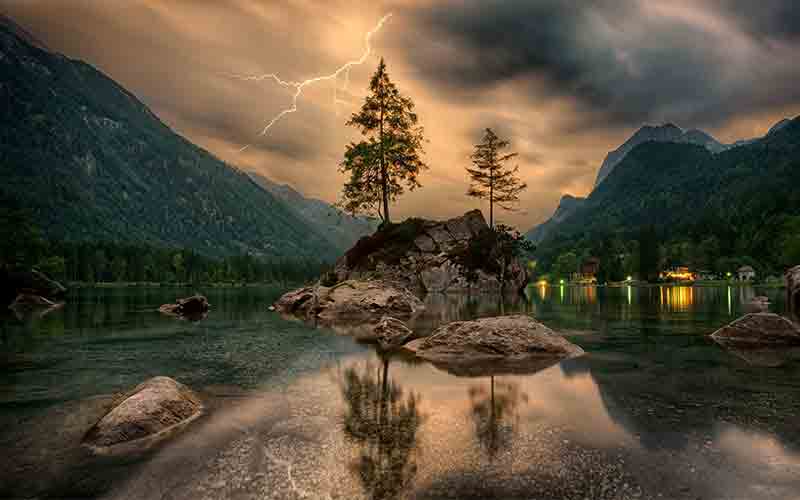 Lightning flashing above a rocky islet with two trees on a calm lake