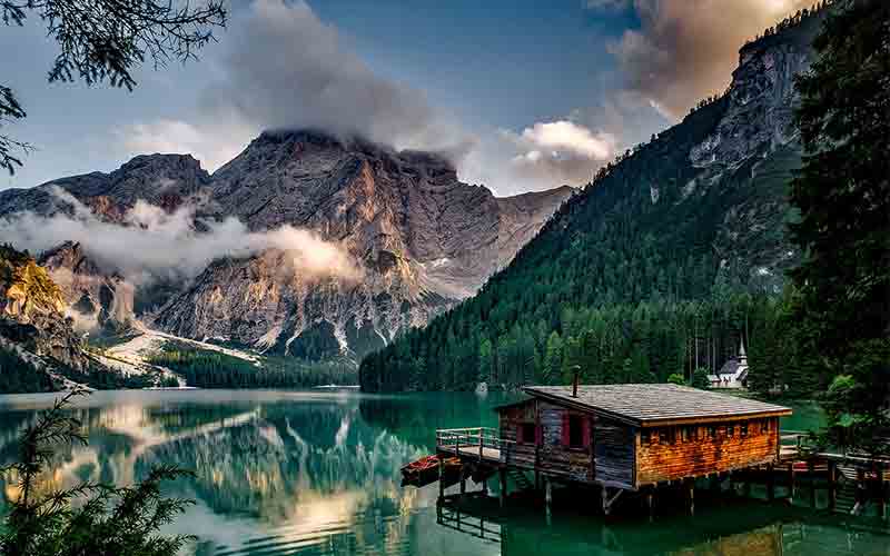 Cloud‑wrapped mountain reflected in a still alpine lake with a wooden boathouse